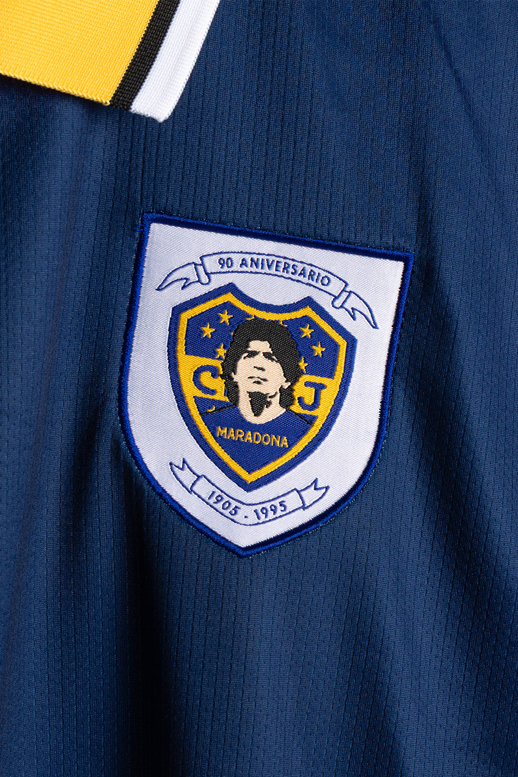 Close-up of a navy blue soccer jersey with a white, yellow, and blue embroidered crest patch on the chest.