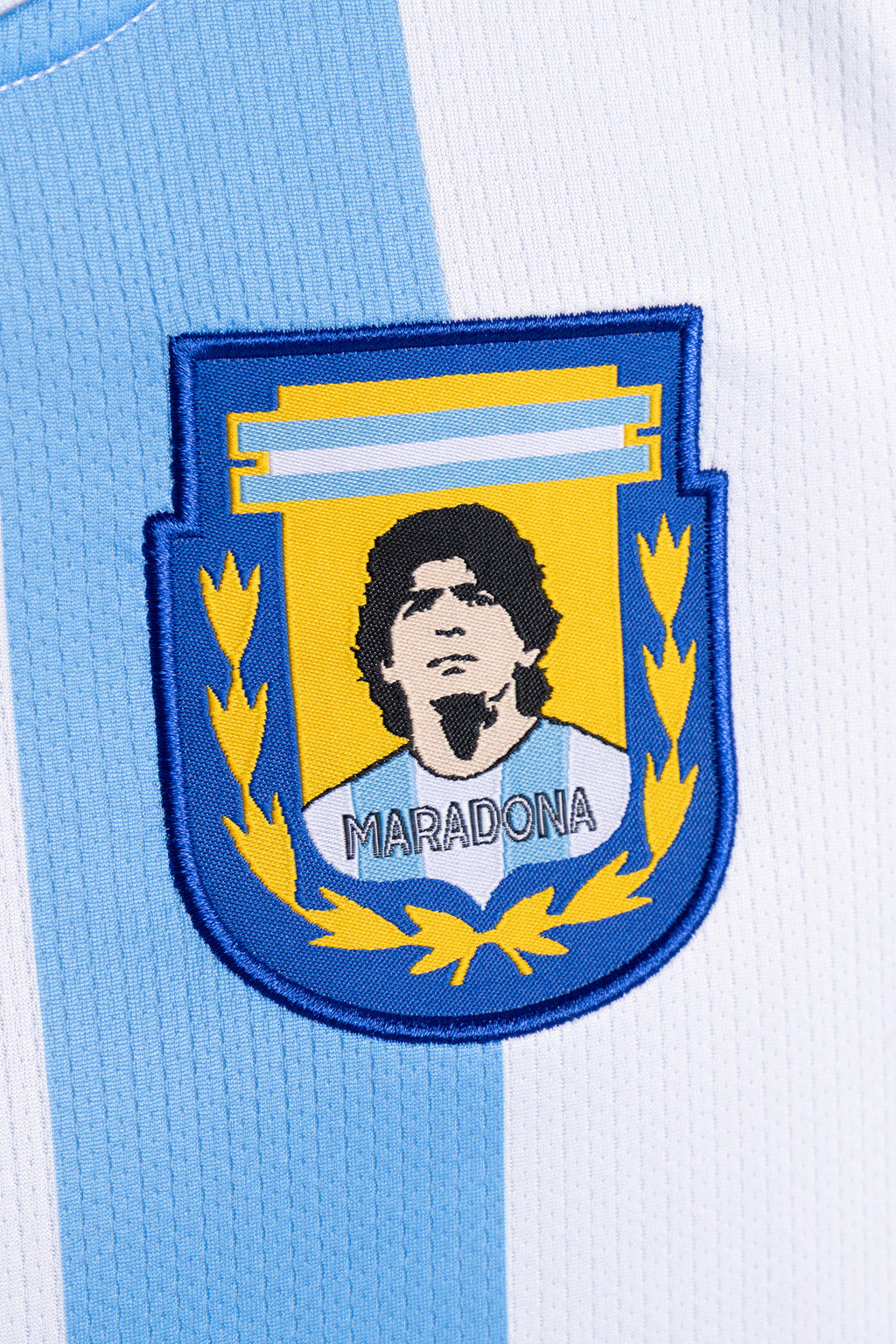 Close-up of a light blue and white striped soccer jersey with an embroidered Argentina national team crest featuring Diego Maradona and the name 'MARADONA'.