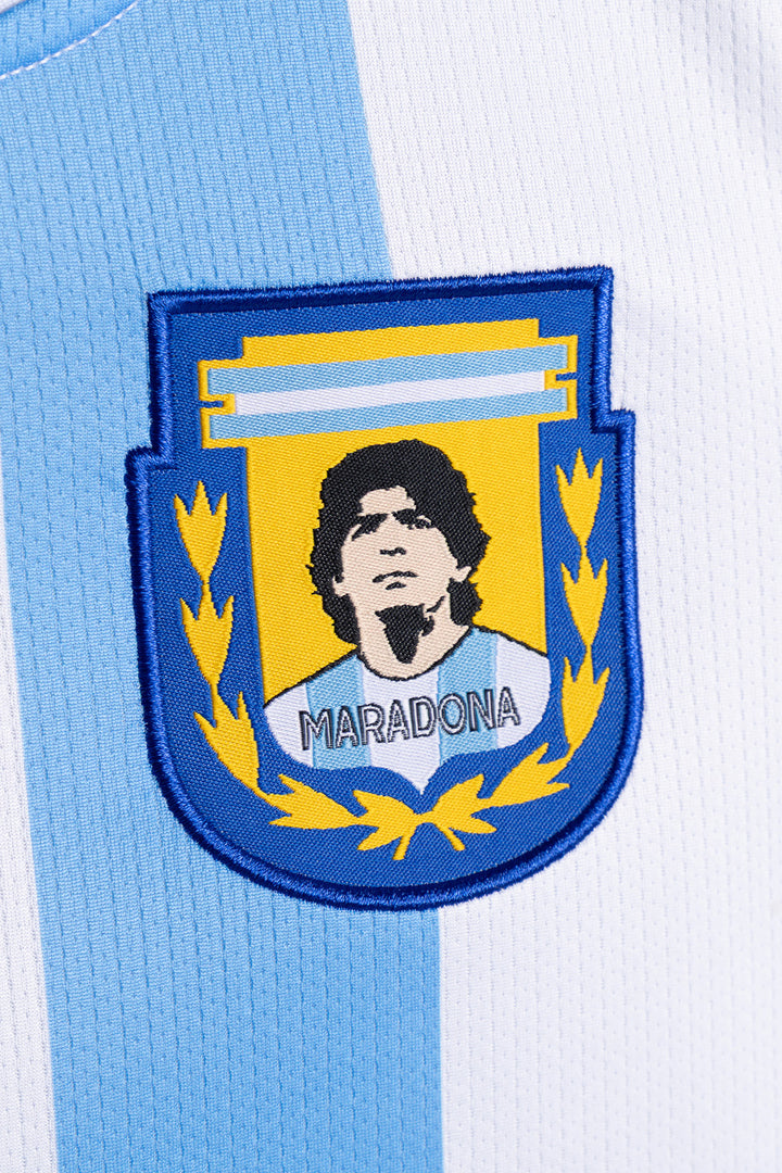 Close-up of a light blue and white striped soccer jersey with an embroidered Argentina national team crest featuring Diego Maradona and the name 'MARADONA'.