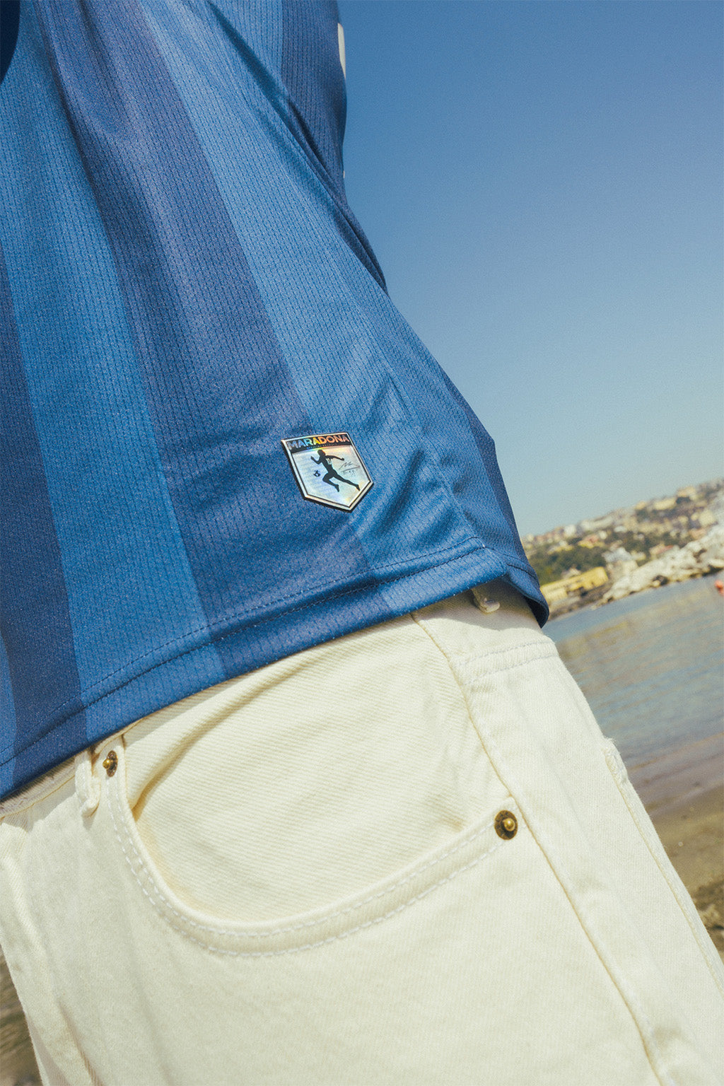 Navy jersey close up with a Maradona logo, with a scenic background of water and buildings.