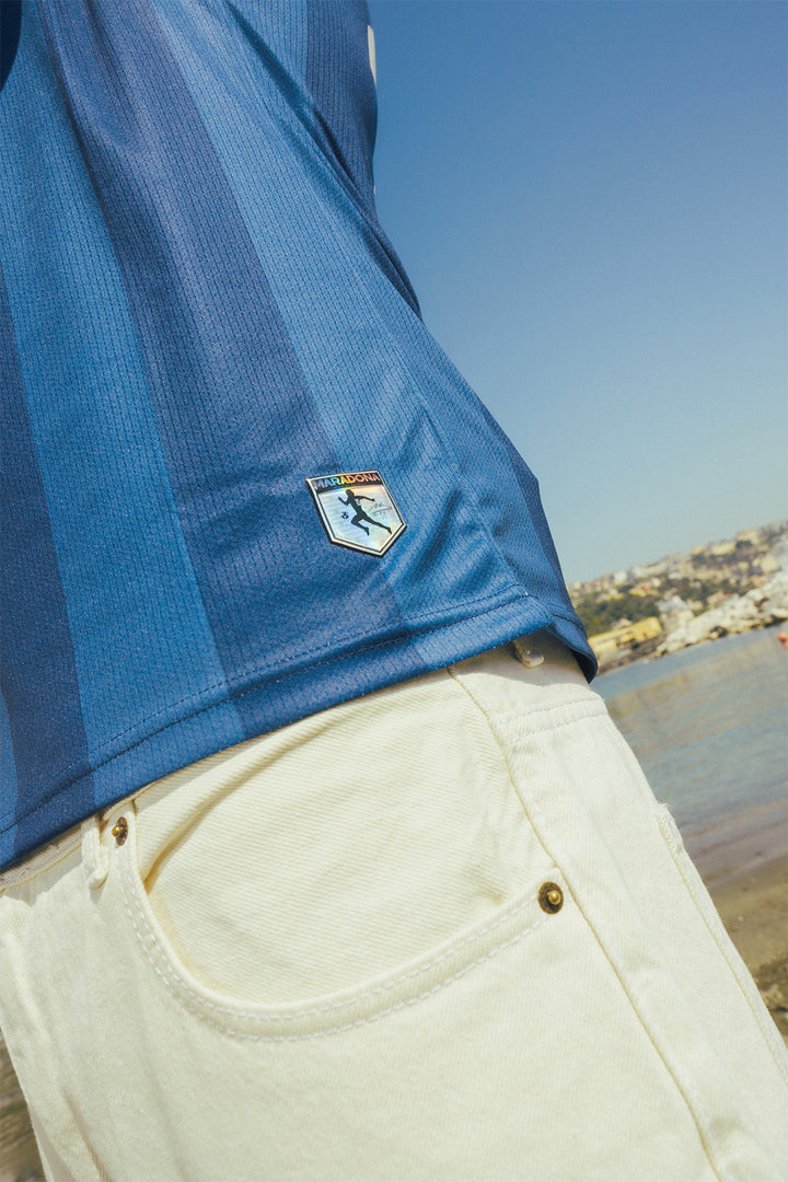 Navy jersey close up with a Maradona logo, with a scenic background of water and buildings.