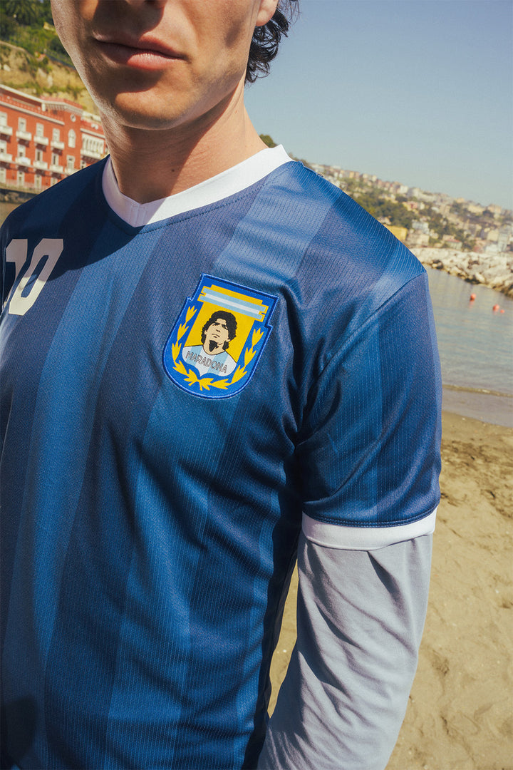 Close up of man wearing a navy sports jersey with a Maradona crest on a beach.