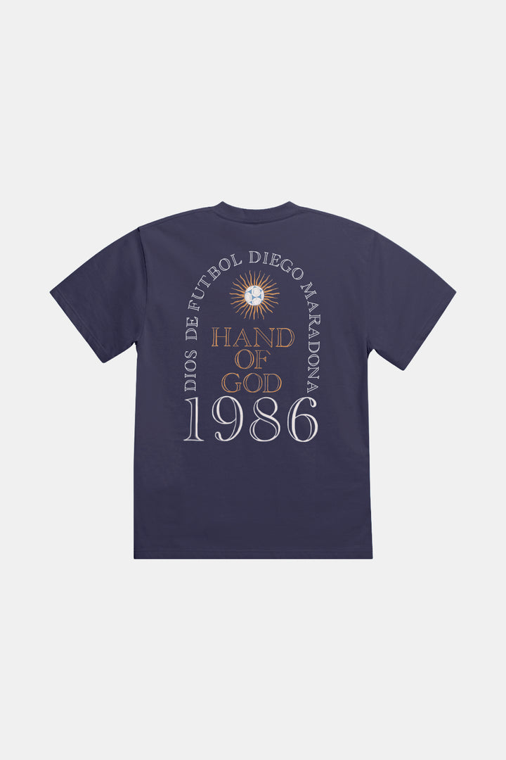 A navy blue short-sleeve t-shirt shown from the back, featuring a circular graphic print with a sunburst, the text 'DIOS DE FUTBOL DIEGO MARADONA', 'HAND OF GOD', and '1986' in white and gold.