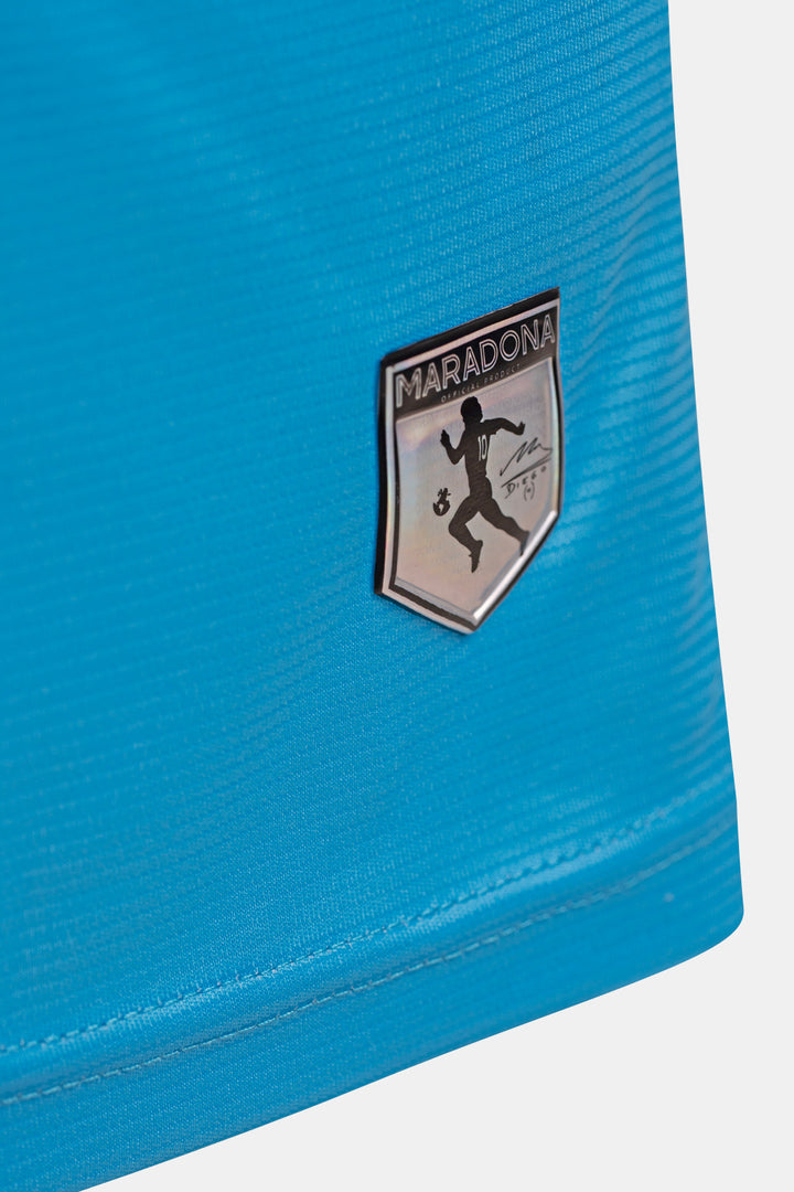 Close-up of a bright blue athletic fabric with a shield-shaped Maradona crest patch on the front.