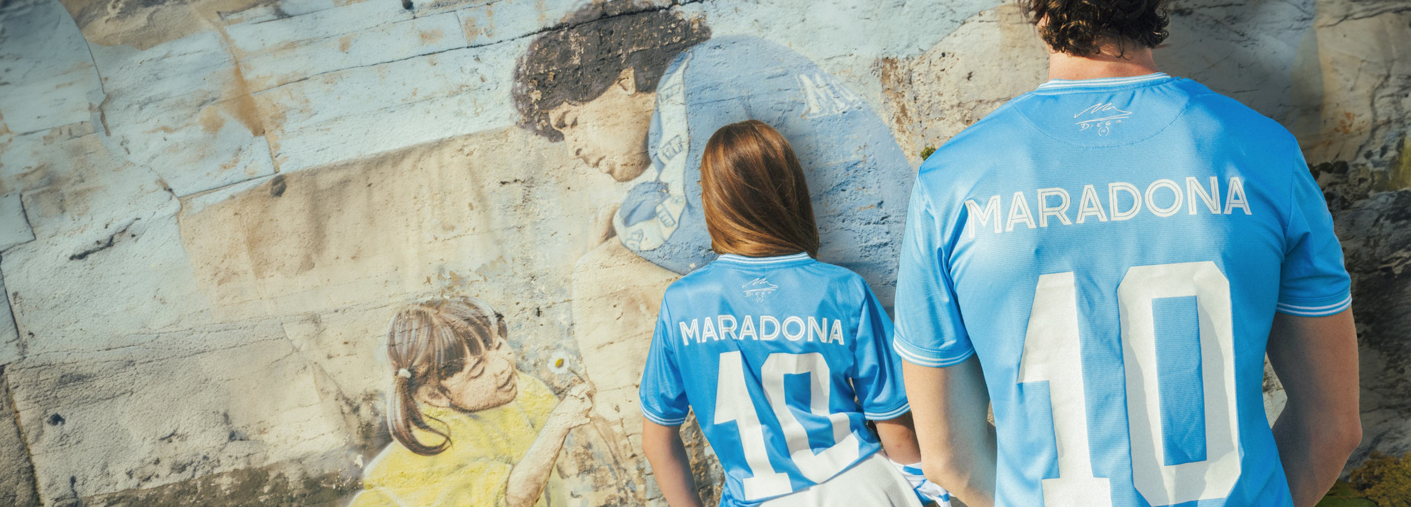 Two people wearing 'Maradona' jerseys standing in front of a mural.
