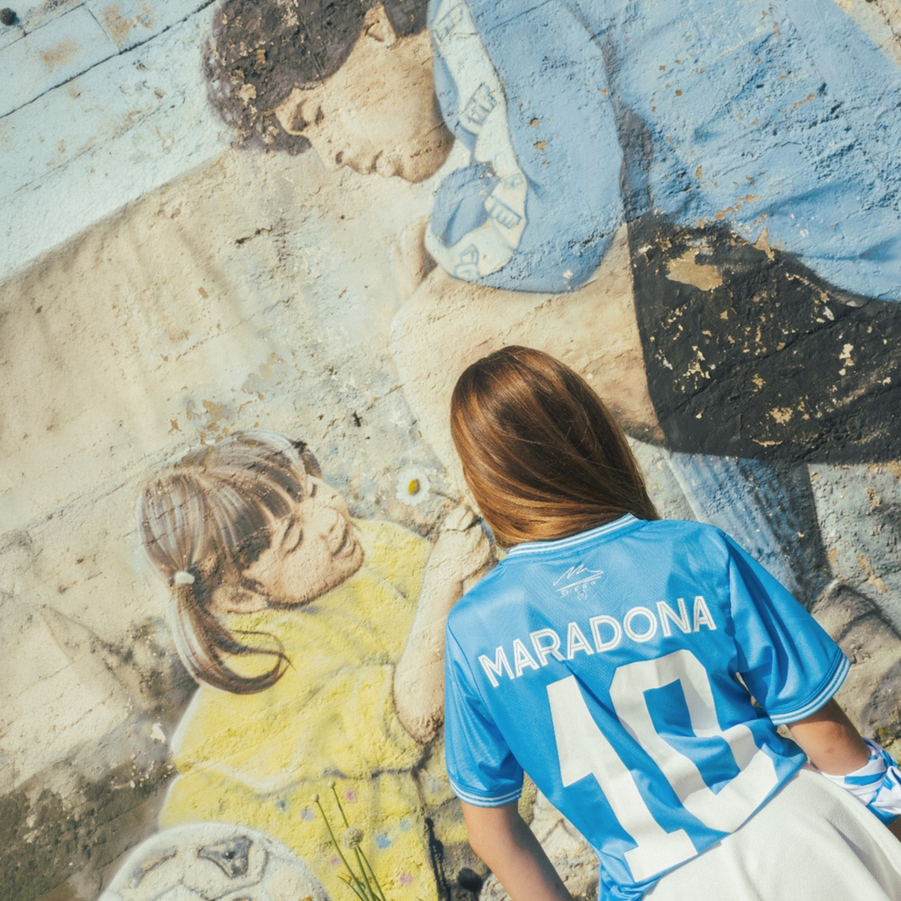 Person wearing a blue Napoli sports jersey with 'Maradona' and number '10', standing in front of a mural.