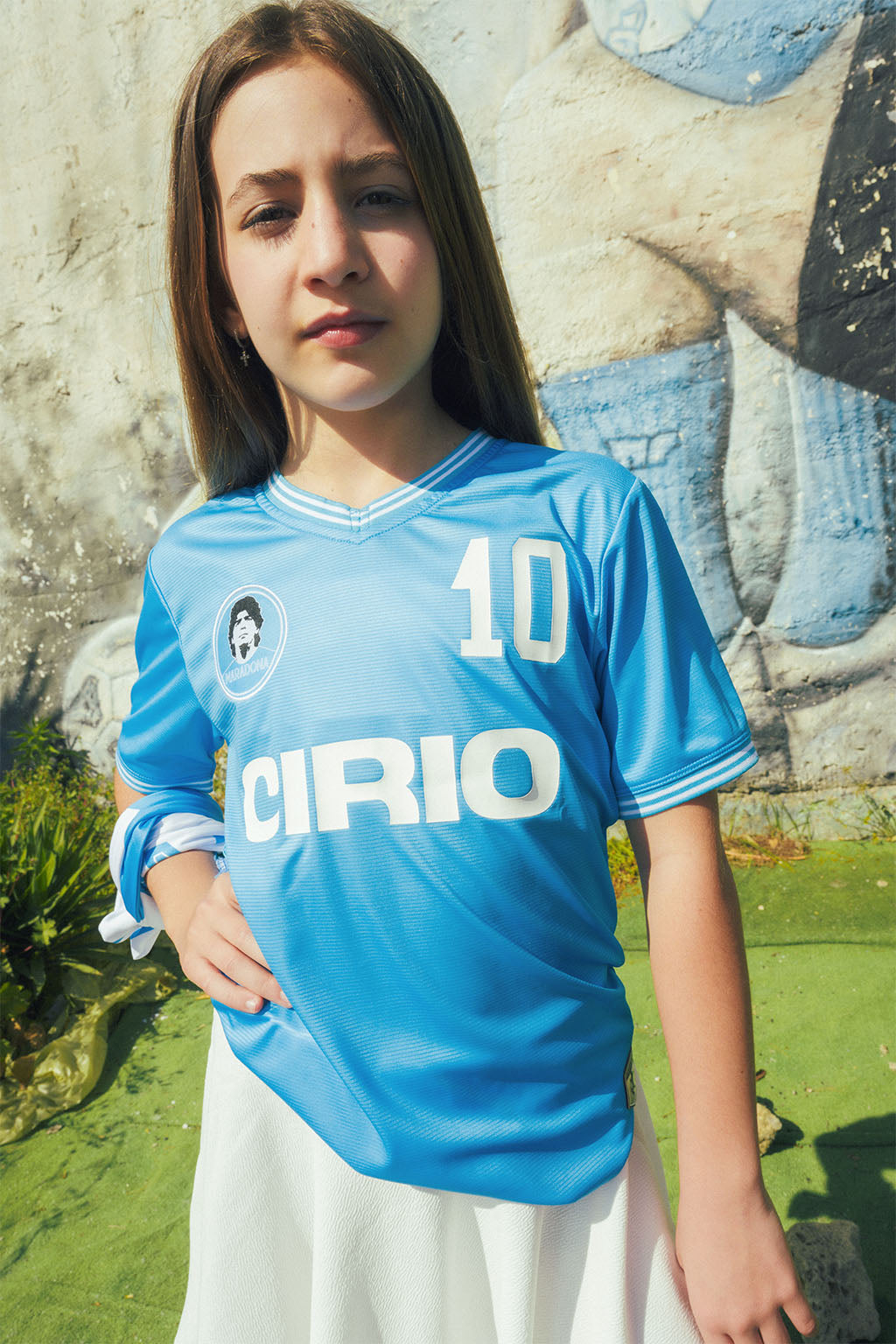Child wearing a blue Maradona replica Napoli sports jersey with 'Cirio' branding in an outdoor setting.