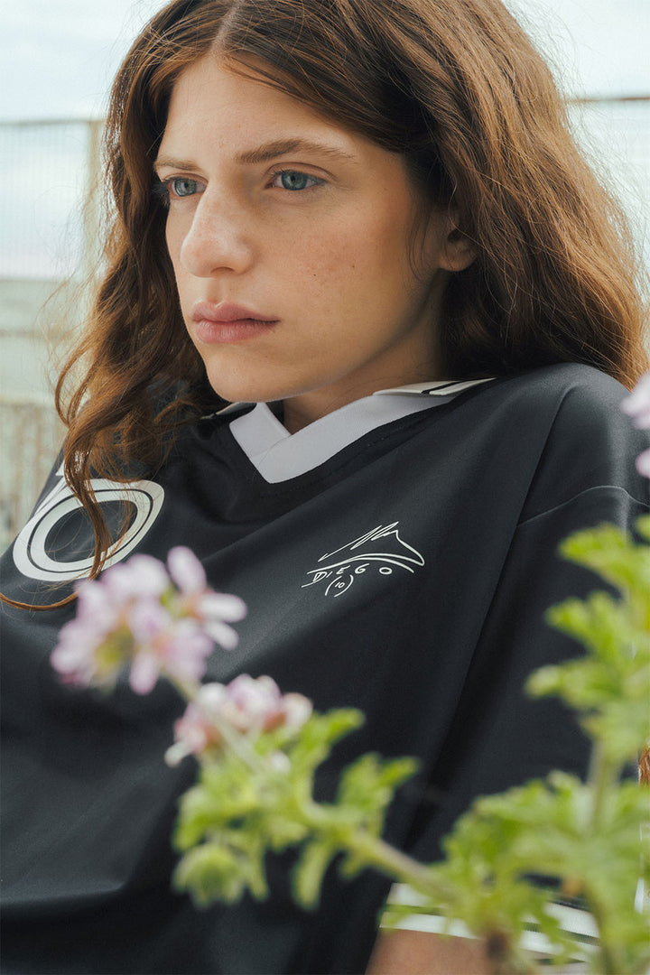 Woman wearing a signature black Maradona replica jersey, sitting among urban flowers