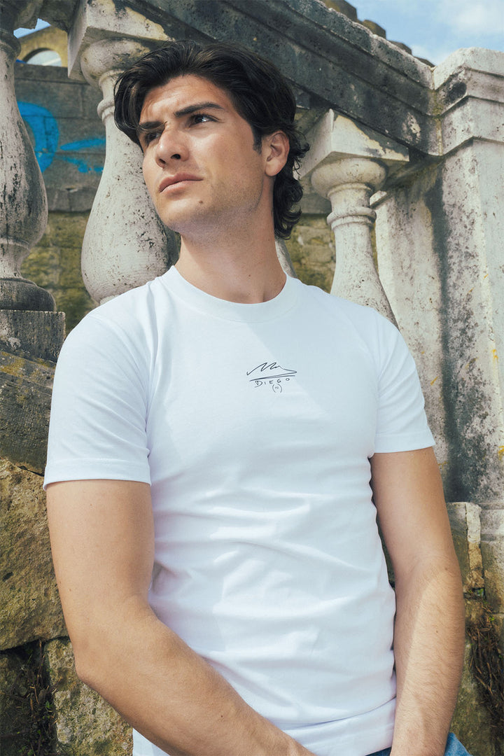 Man wearing a white t-shirt with a Maradona signature logo in front of stone staircase
