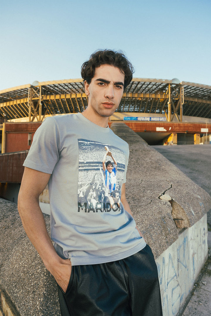 Man wearing a t-shirt with a graphic Maradona 86 design outside stadium