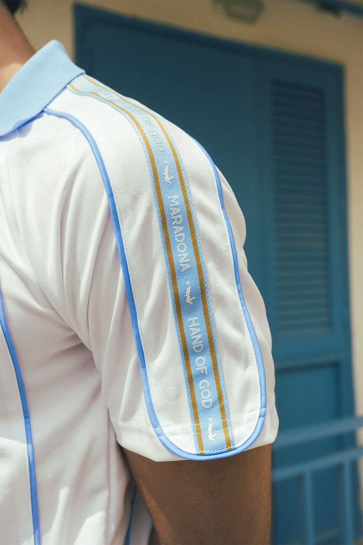 Close-up of a man wearing a white jersey with blue and gold accents, standing in front of a blue door.