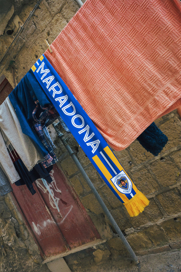 Maradona Boca inspired scarf with blue and yellow design hanging in front of a brick wall