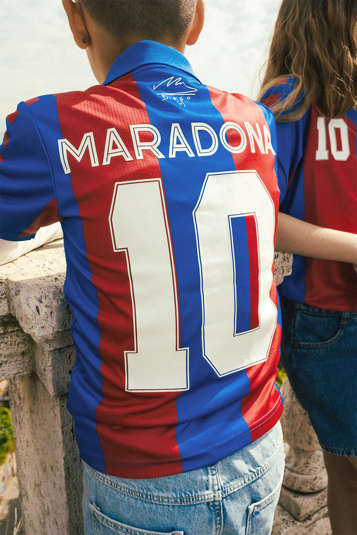 Two kids wearing red and blue replica Barcelona jersey with 'Maradona' and number '10' on a stone balcony.
