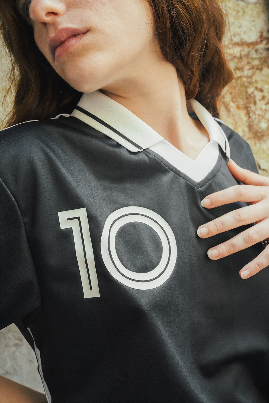 Woman wearing a signature black Maradona replica jersey with the number 10 on a textured stone wall background