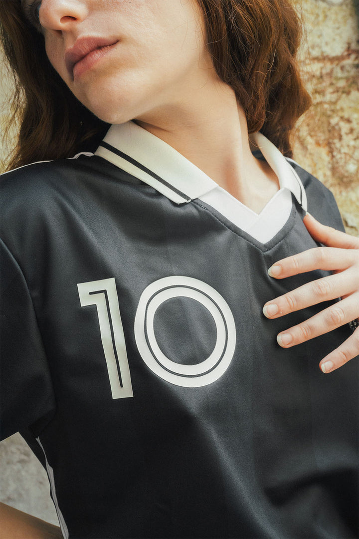 Woman wearing a signature black Maradona replica jersey with the number 10 on a textured stone wall background
