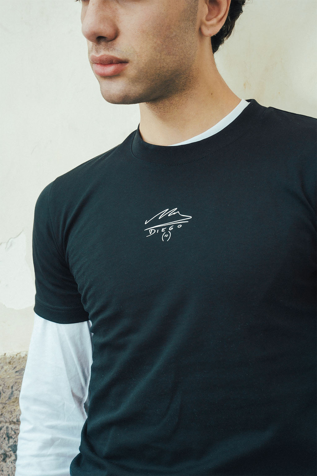 Man wearing a black t-shirt with a Maradona signature logo on a light stone background