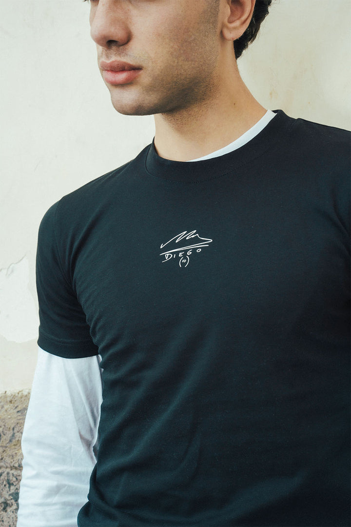 Man wearing a black t-shirt with a Maradona signature logo on a light stone background