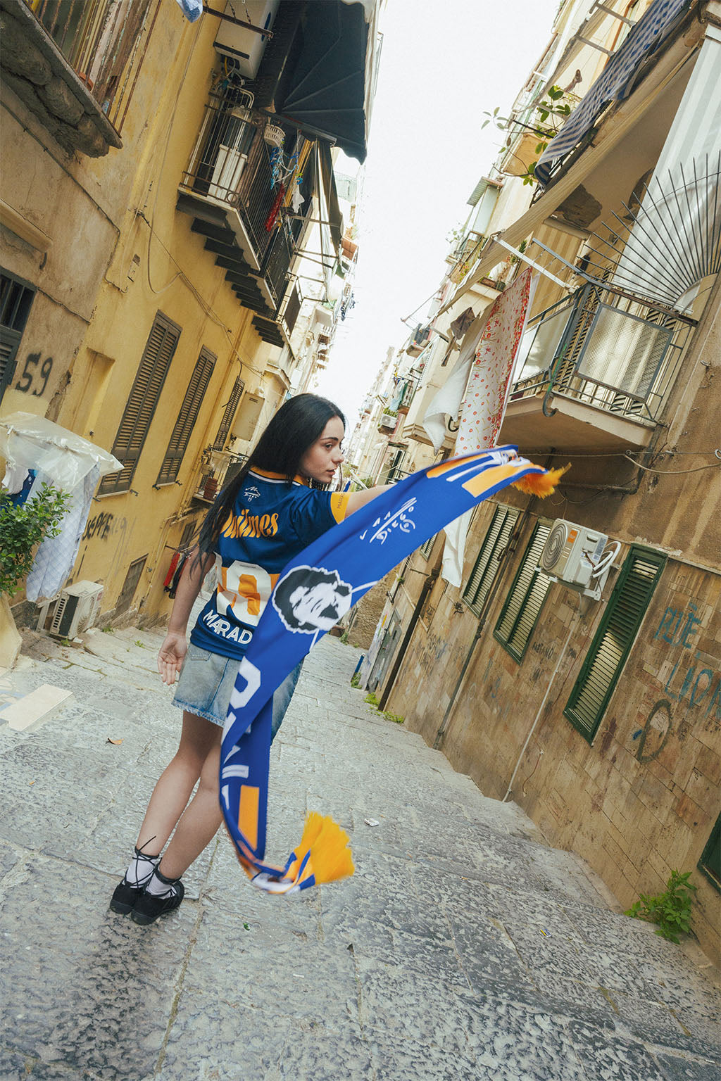Woman holding a Boca inspired Maradona scarf in an stone urban alleyway.