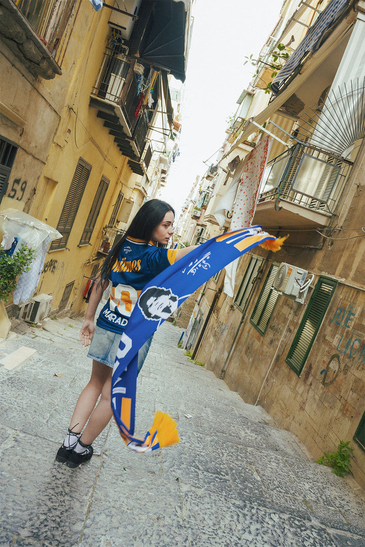 Woman holding a Boca inspired Maradona scarf in an stone urban alleyway.