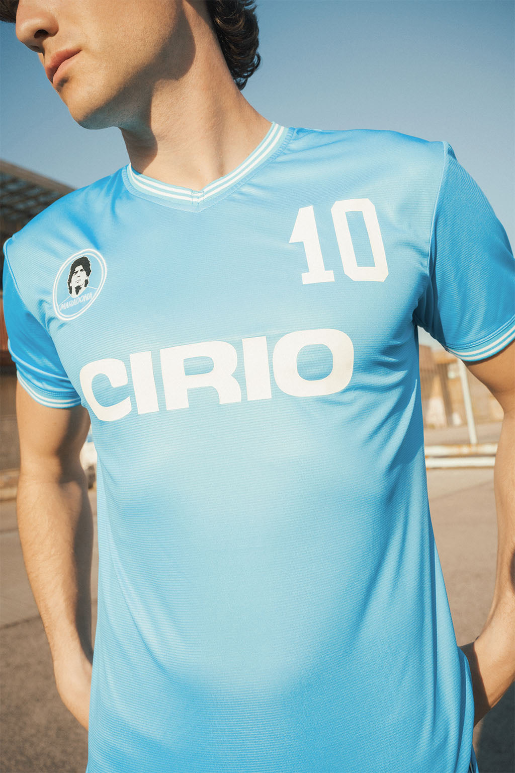 Close up of man wearing a light blue Napoli replica 86 sports jersey with Maradona branding and number '10'.