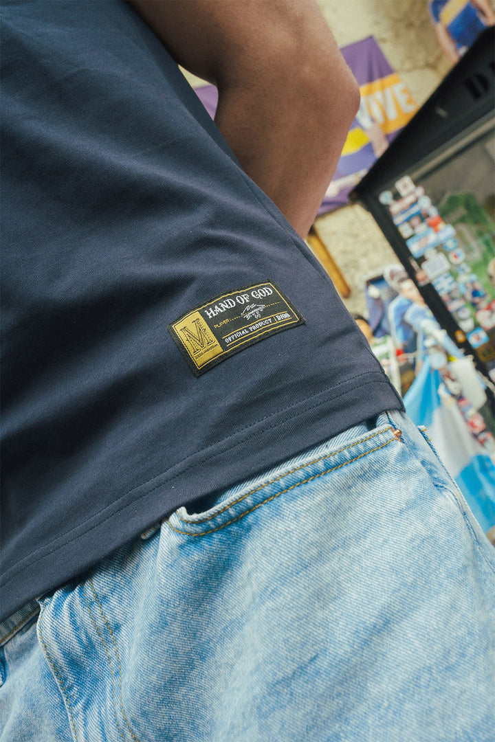 Close up of man wearing a navy blue shirt with a Hand of God label, standing in a Maradona stand.