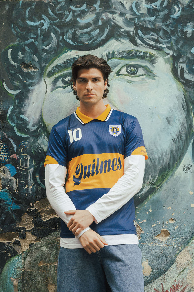 Man wearing a blue and yellow Boca jersey with Maradona graphic in front of a mural.