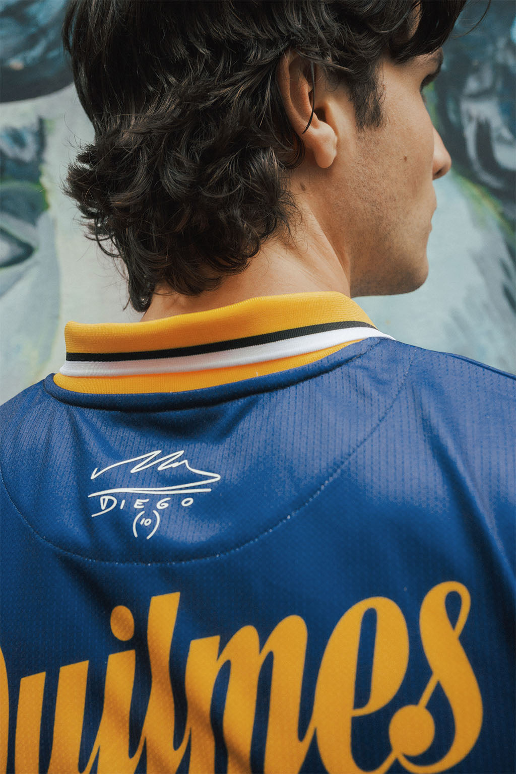 Close up man wearing a blue and yellow Boca jersey with Maradona signature, standing against a blurred background.