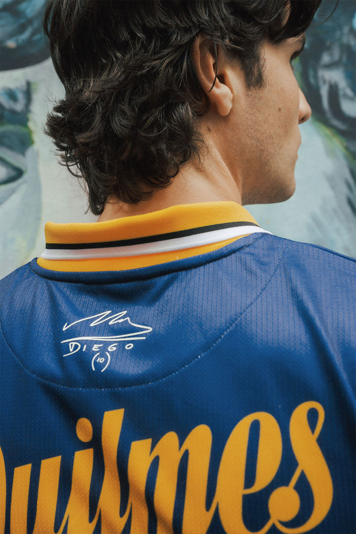 Close up man wearing a blue and yellow Boca jersey with Maradona signature, standing against a blurred background.